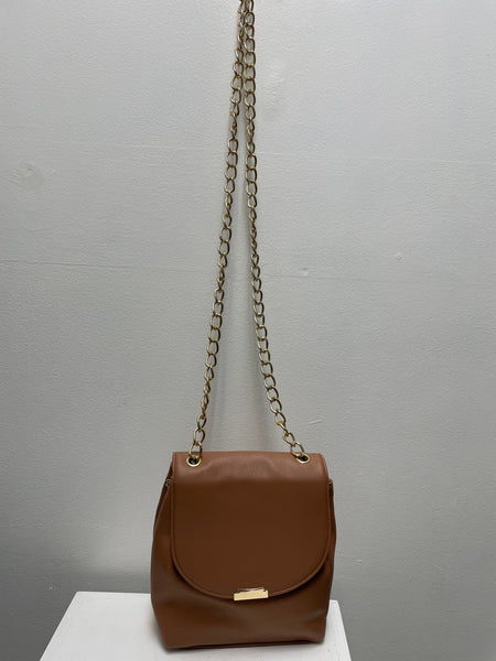 Tan vegan leather crossbody bag with flap closure and gold chain strap hanging on a wall