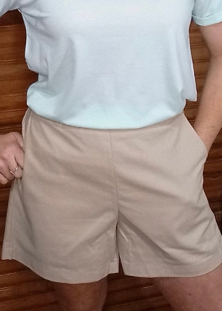 A woman wearing high-rise beige shorts with front pockets, paired with a pale blue top.