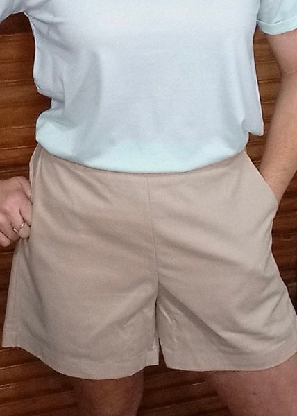 A woman wearing high-rise beige shorts with front pockets, paired with a pale blue top.