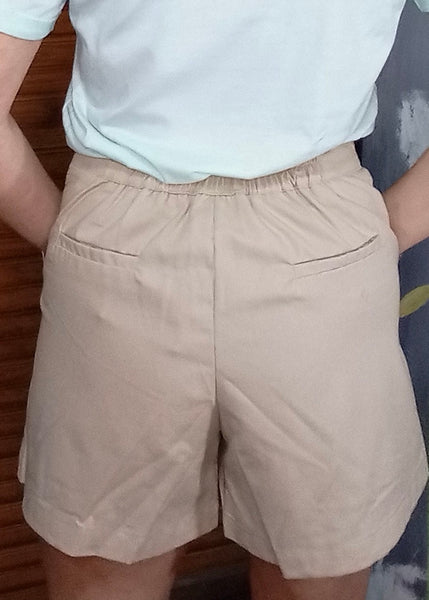 A woman wearing high-rise beige shorts with front pockets, paired with a pale blue top.