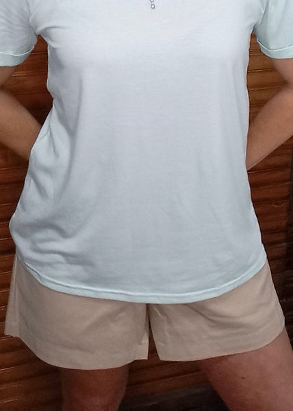 A woman wearing high-rise beige shorts with front pockets, paired with a pale blue top.