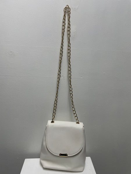 White vegan leather crossbody bag with flap closure and gold chain strap hanging on a wall