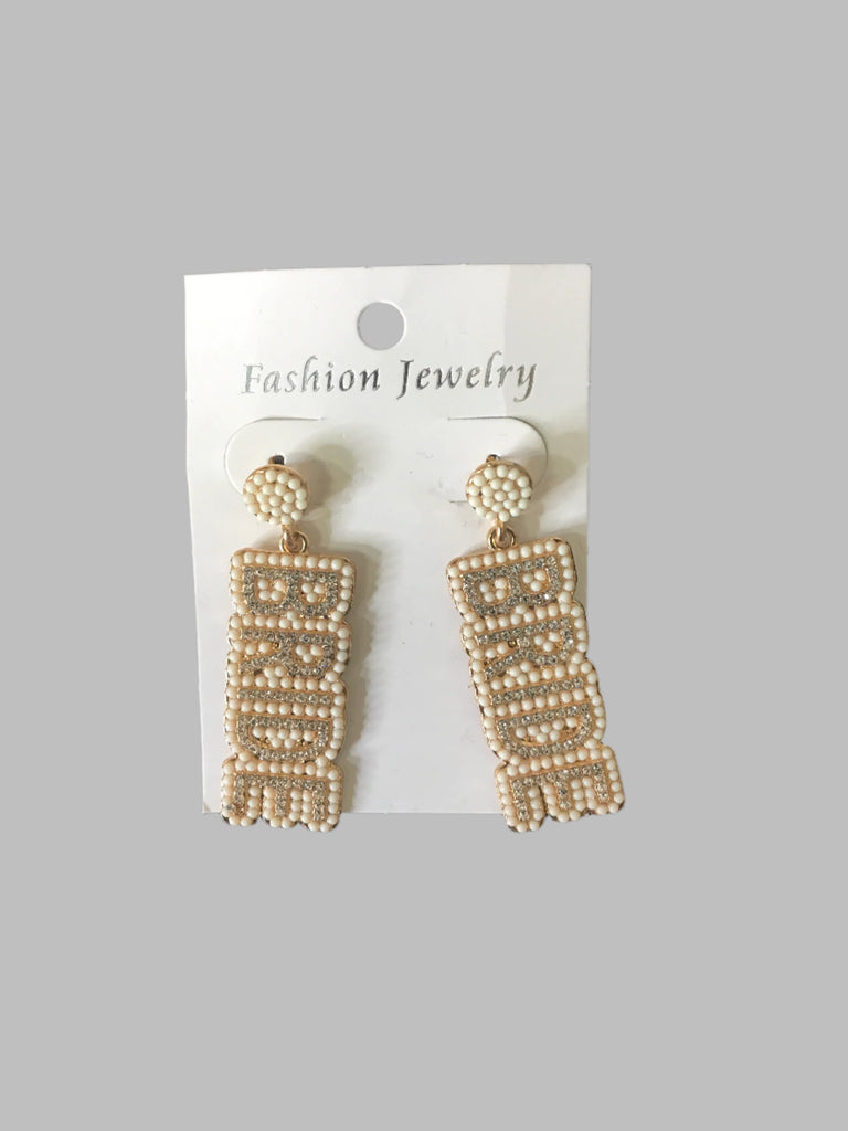 Beaded “BRIDE” statement earrings in cream and gold tones displayed on a jewelry card.
