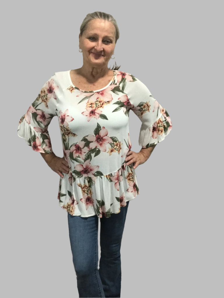 Woman wearing a white floral ruffle hem top with 3/4 bell sleeves, paired with jeans, standing against a neutral background.