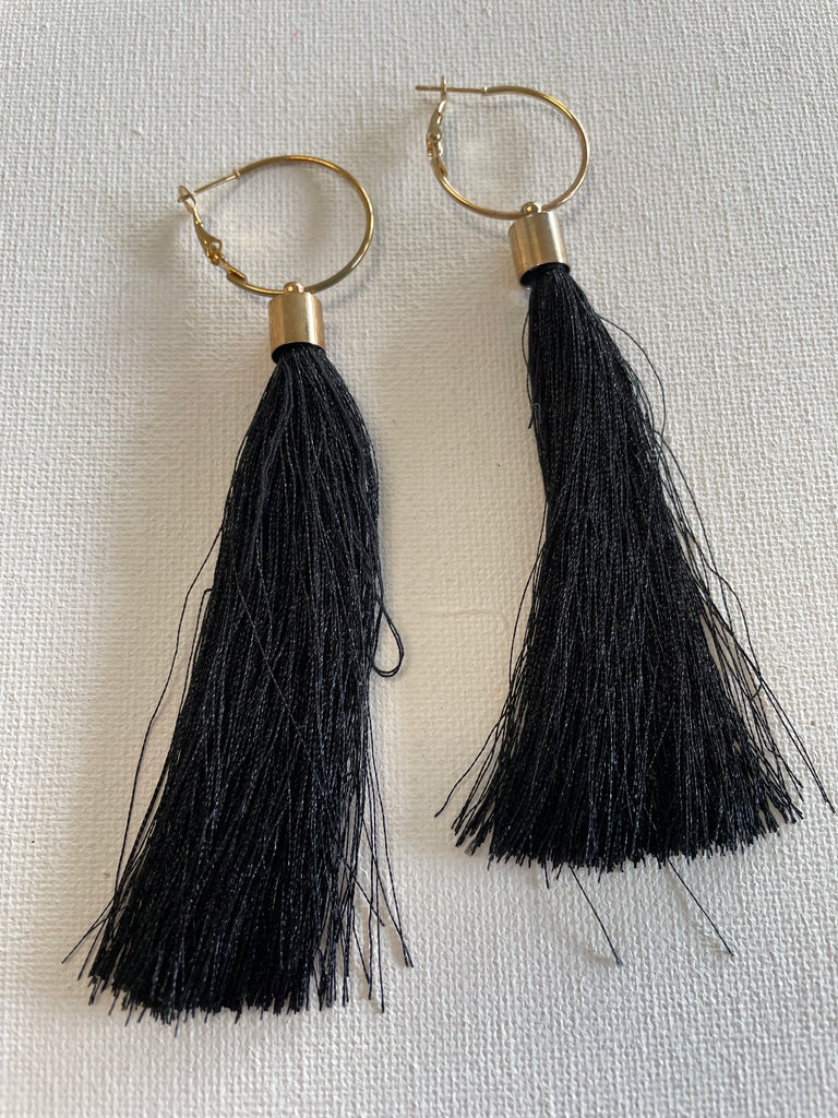 Black tassel earrings with gold hooks on a light gray background