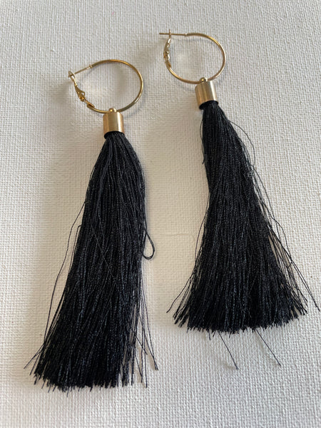 Black tassel earrings with gold hooks on a light gray background
