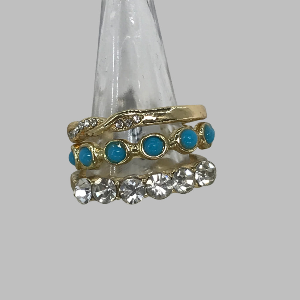 Rings: Set of 3. Top ring is gold with diamond shaped stones. Second ring is gold outlined with a blue center. Third ring is gold interweaved with small diamond shaped strands