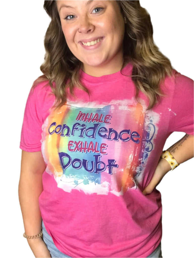 Pink sublimated shirt that says "inhale confidence exhale doubt" on colorful back ground