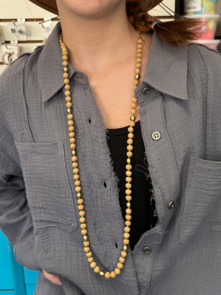 A long beaded necklace featuring natural wood beads accented with gold spacers, styled over a textured gray button-up shirt.