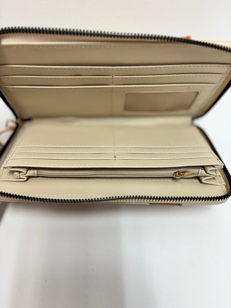 A the inside of a neutral beige and tan crossbody wristlet with whipstitch accents and gold-tone hardware, photographed on a clean white background