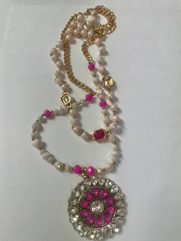 Gold double chain necklace with white beads and a round pendant featuring clear rhinestones and pink stones, displayed on a white background.