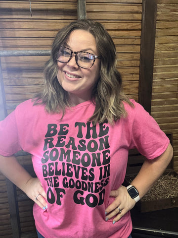 Pink Shirt with black lettering quoting "Be the reason someone believes in the goodness of god.