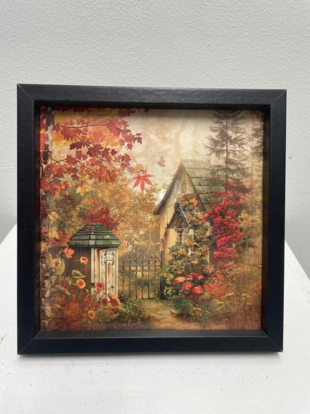 Framed artwork of a garden scene with a small cottage and autumn foliage.