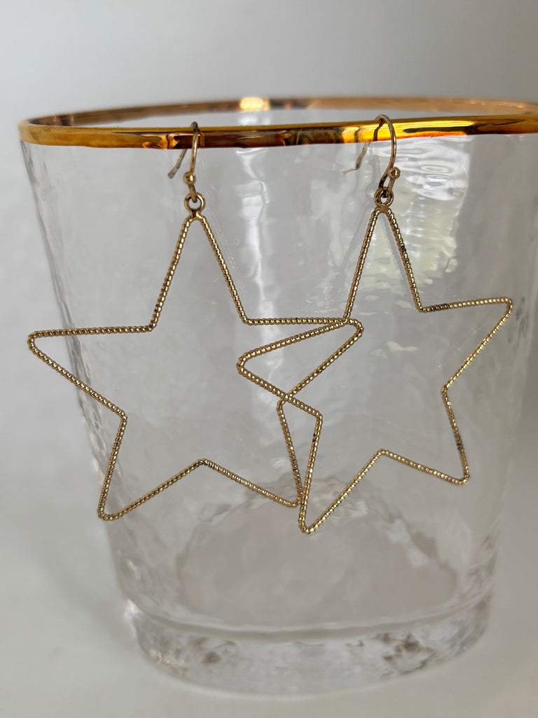 Open Star pierced earrings in goldtone metal hanging on a glass with a with background