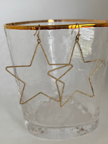Open Star pierced earrings in goldtone metal hanging on a glass with a with background