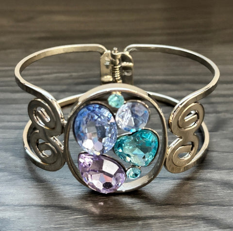 Silver-tone hinged bangle bracelet with swirl sides and multicolor faceted crystals in blue, aqua, and purple