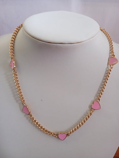 A gold chain necklace with five pink heart charms trimmed in gold displayed 
