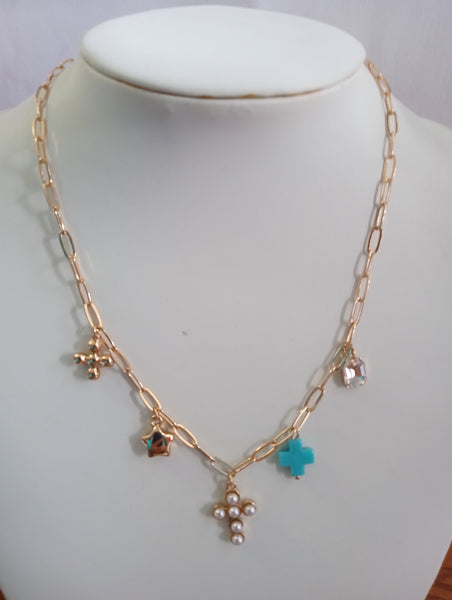 A gold-toned chain necklace, featuring multiple charms including a turquoise cross, a pearl cross, a small brown star, and clear rhinestone accents.