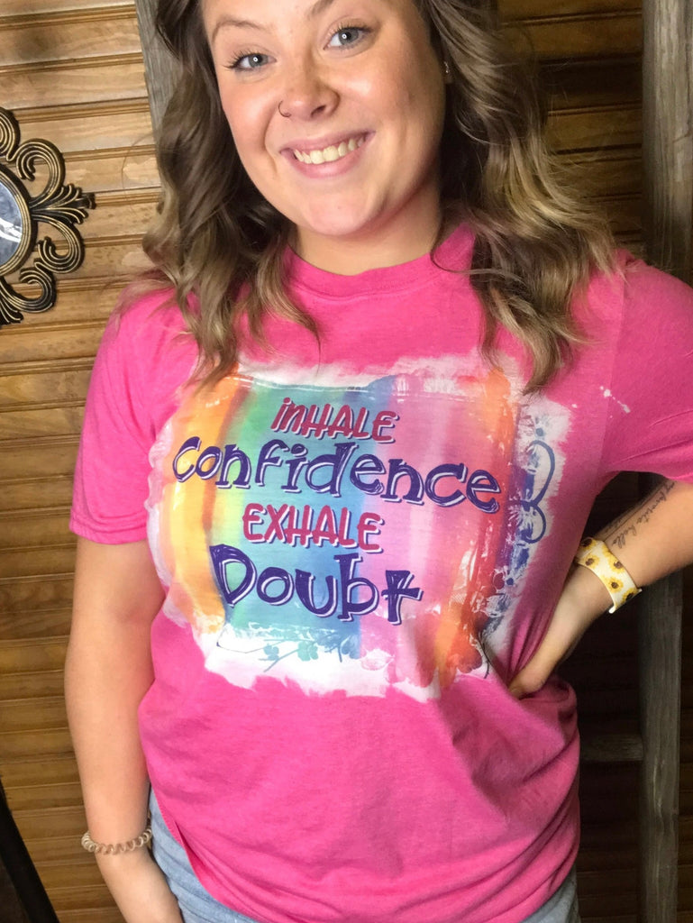 Pink sublimated shirt that says "inhale confidence exhale doubt" on colorful back ground