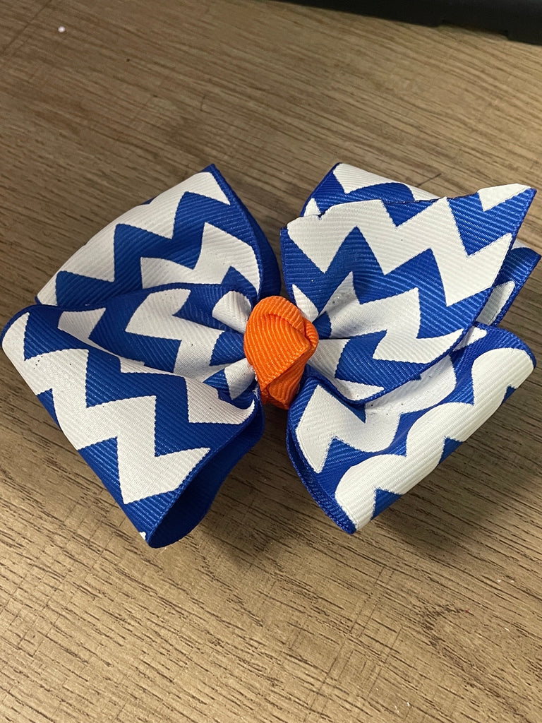 Blue and white chevron patterned hair bow with an orange center on a wooden surface.