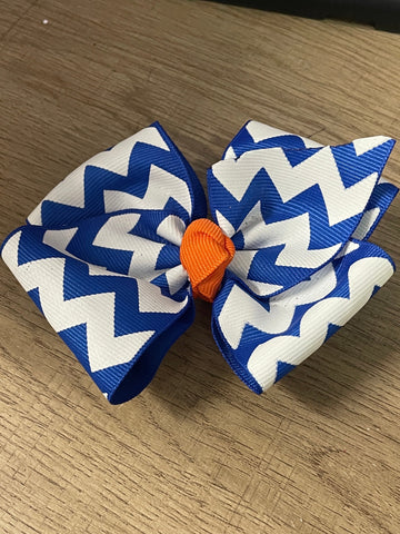 Blue and white chevron patterned hair bow with an orange center on a wooden surface.