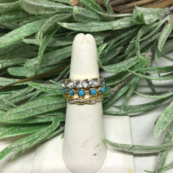 Rings: Set of 3. Top ring is gold with diamond shaped stones. Second ring is gold outlined with a blue center. Third ring is gold interweaved with small diamond shaped strands 