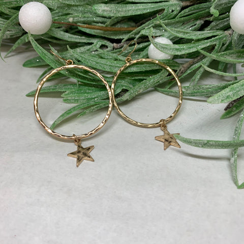 Gold pierced earrings with a large round hammered gold hoop featuring a small gold star.