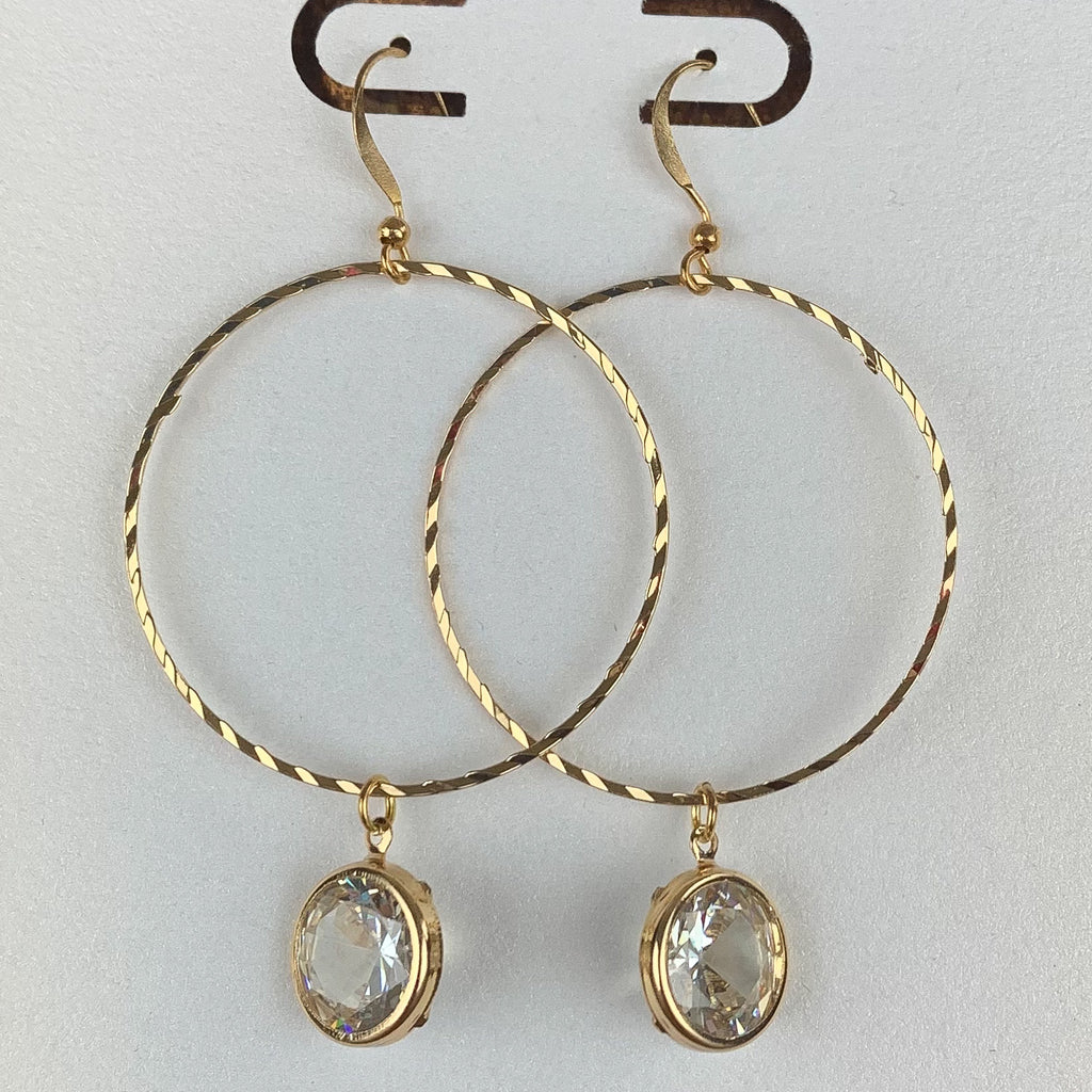 Pierced gold earrings with a large gold hoop featuring a crystal drop outlined in gold. 