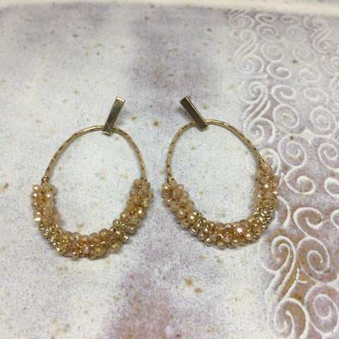Pierced earrings with gold oval hoop with gold pearl beads on bottom half of hoop. 