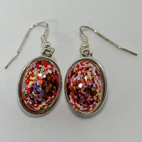 Silver pierced earrings with large silver oval with sparkle glitter on the inside. Sparkle colors are pink, red, and gold. 